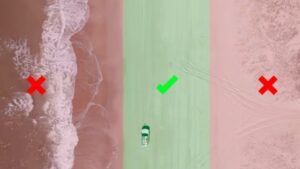 Aerial shot of a 4WD driving on the beach with a green safe zone and red danger zones